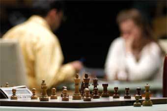 Вишванатан Ананд и Юдит Полгар на фоне шахматной доски с фигурами. Фото с официального сайта турнира